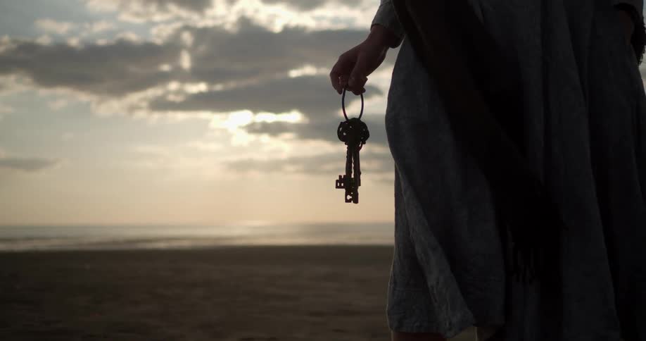 A woman holds a ring of keys while standing on a beach