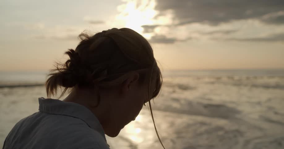 A woman in a beach looking down with the ocean and the sky in the background