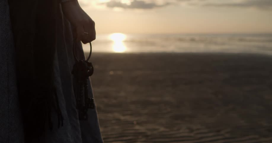 A woman stands on the beach holding a large set of keys