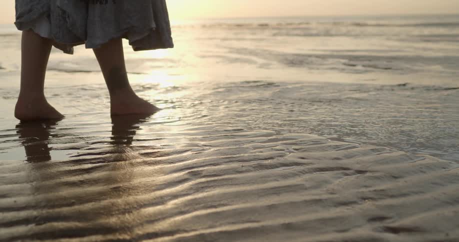 A woman walks to the ocean and drops a handful of keys into the water