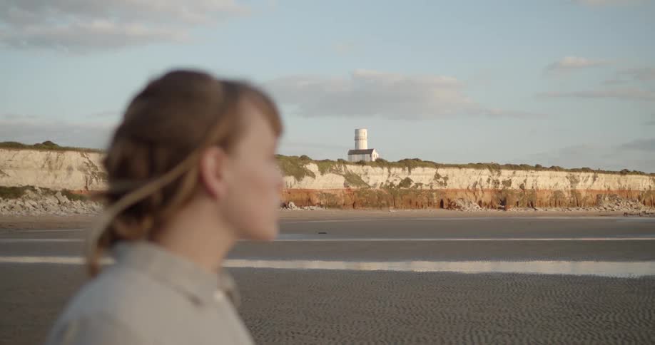 Woman stands on a beach near a lighthouse