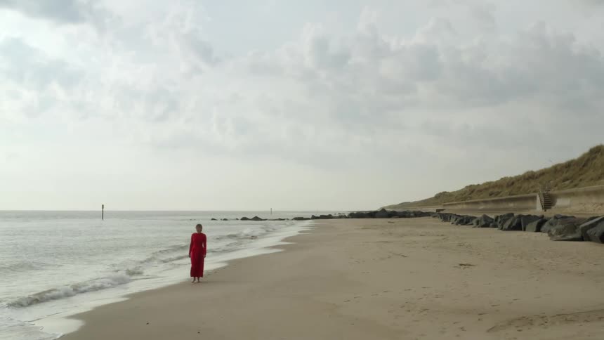 A woman in a red dress walking on a sandy beach with the sky in the background