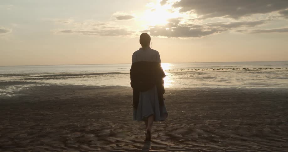 Barefoot woman walks on the sands of a beach at sunset