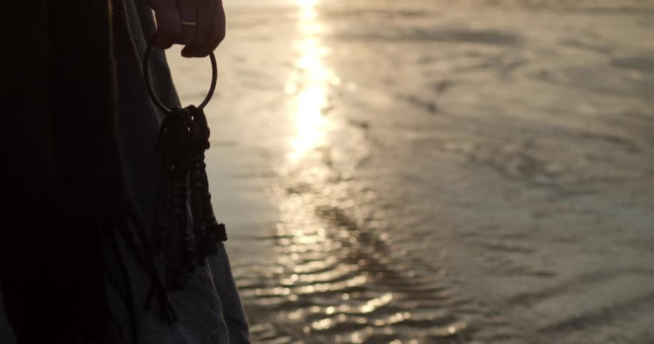 A white woman carries a ring of keys across a watery beach