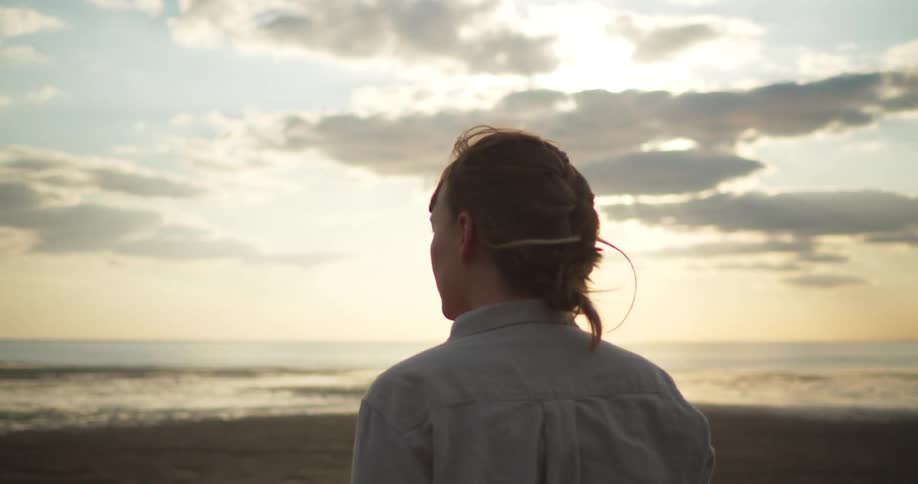 A young woman stands on the beach and looks out at the ocean