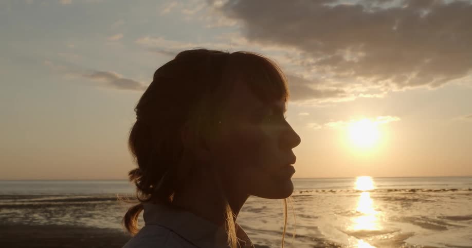 A woman standing on the beach with a sun set and the sky in the background
