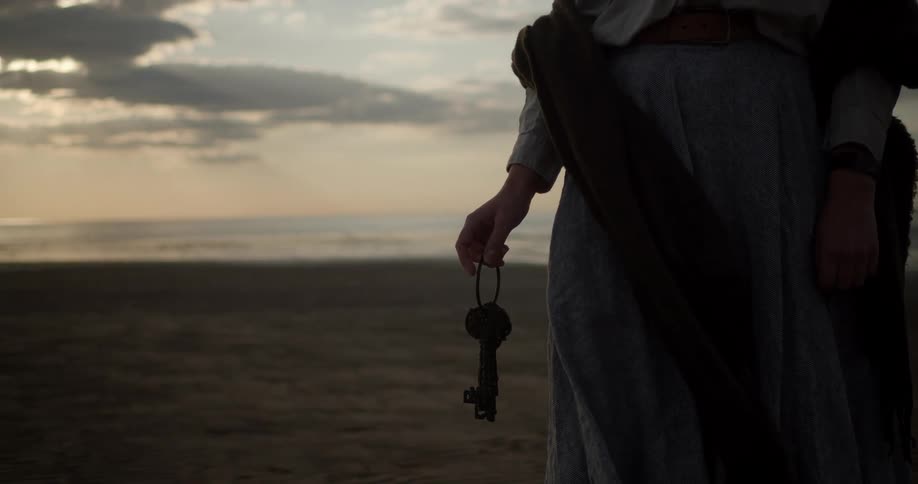 Woman holds key ring with antique keys in a beach at sunset