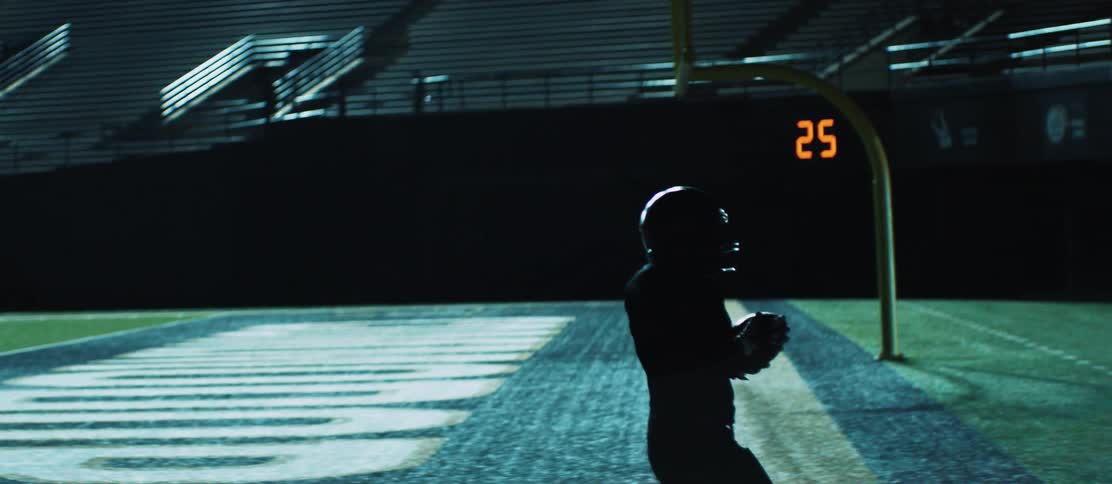 A football player scores a touchdown while playing in an empty stadium at night