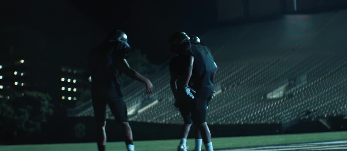 Three black football players slap hands and walk off a stadium field