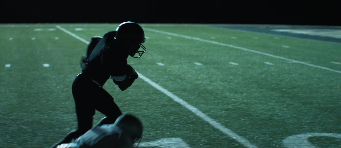 A football player breaks a tackle and runs the ball into an end zone during a night game in a stadium
