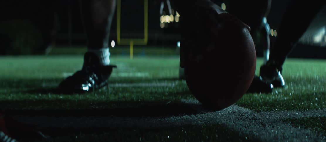 A football team executes a play in a stadium at night