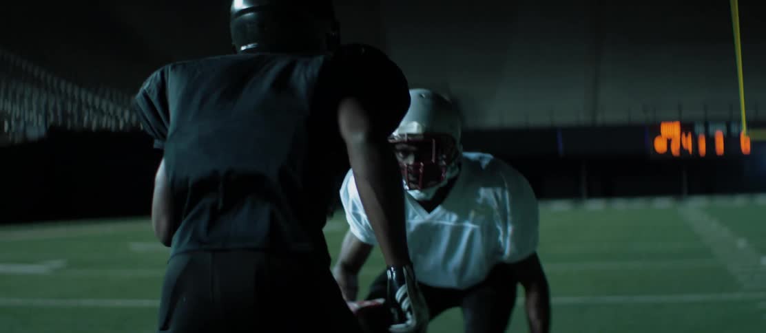 Football players practice in a stadium at night