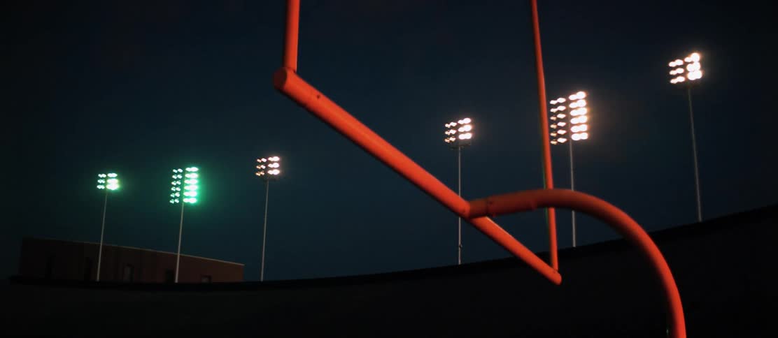 A row of lights in a football stadium turn on at night