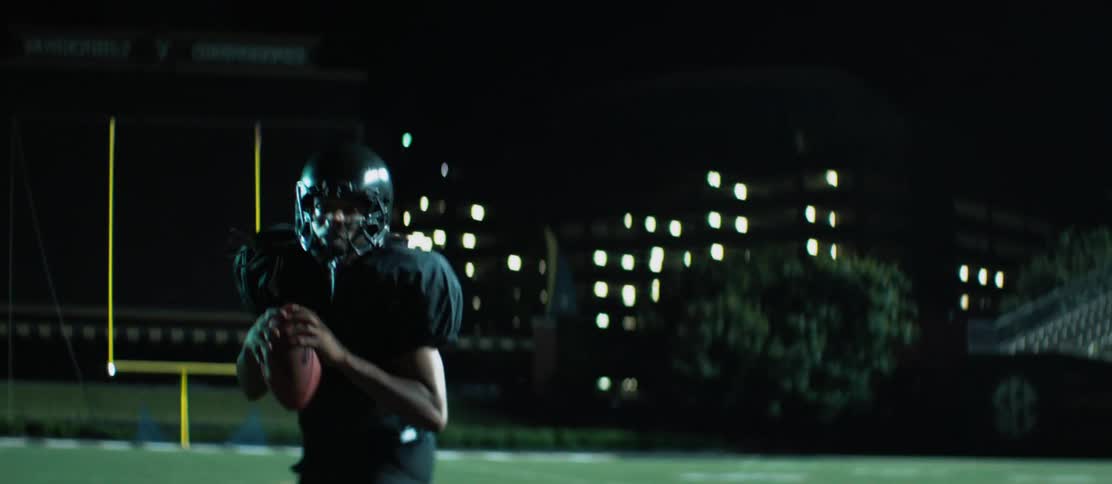A person throws a football to a black teenager and he runs forwards with it