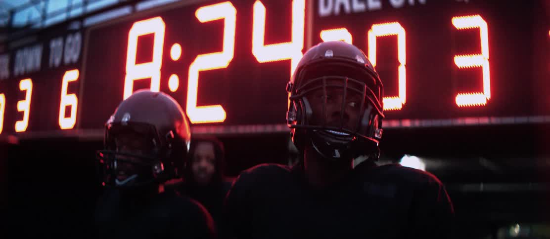 Three black football players stand on a field outside of a tunnel