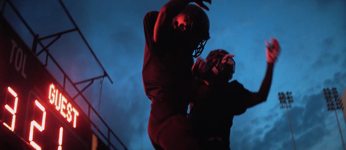 Football players at a stadium slap hands and jump up and body slam one another