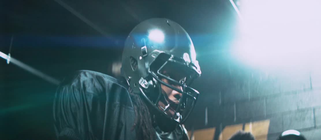 Football players walk along tunnel leading toward field putting on helmets