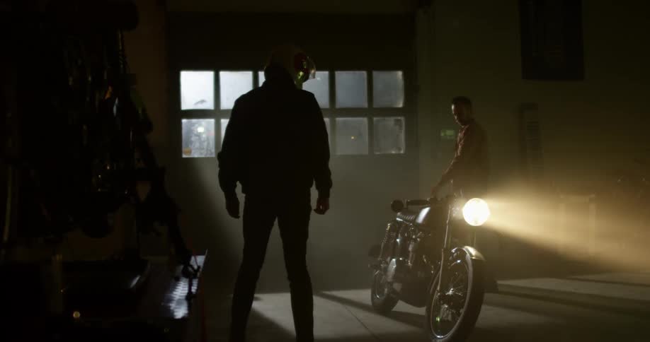Two men look at a motorcycle in a dark garage