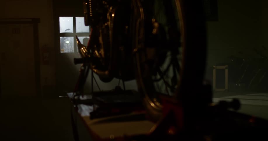 A motorcycle sits on a stand on a table as a man walks by in the distance