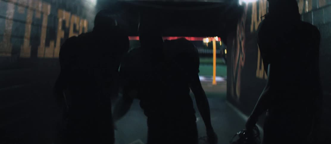 Three black football players walk through a tunnel to get to the field