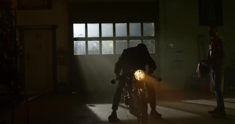 A man takes off his helmet and turns off his motorcycle thats parked in a garage