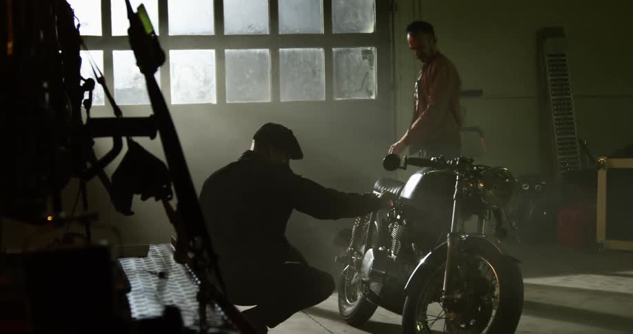 Two white men examine a motorcycle in a garage