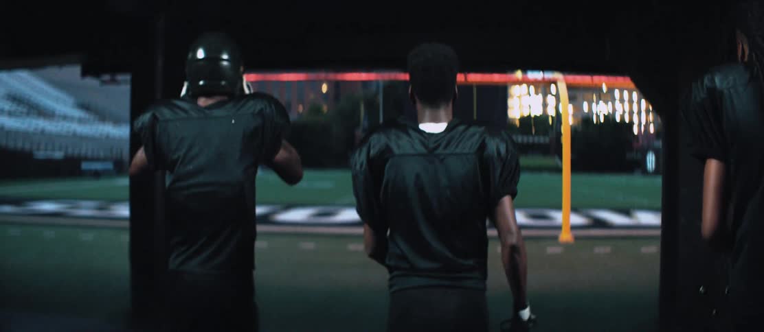 Three men with football helmets and gloves walking towards a football field