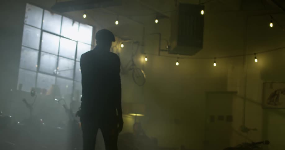 A white man walks across a room containing a motorcycle