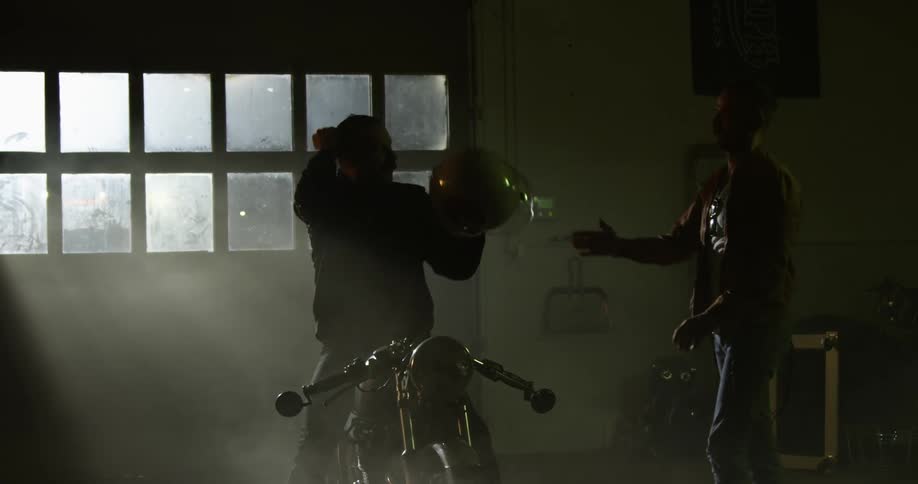 A man removes his motorcycle helmet and hands it to someone