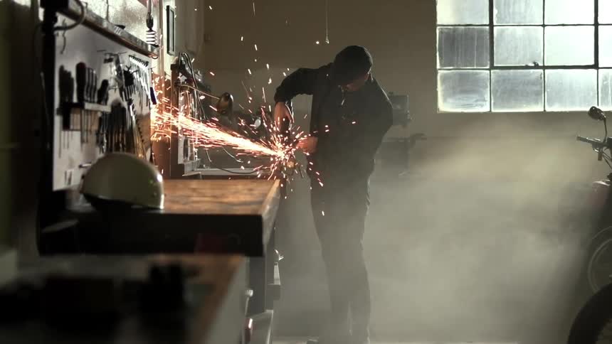 Man cuts metal with a power tool in a workbench inside a workshop