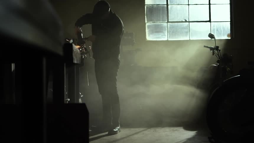 A man welding in a room with a motorcycle