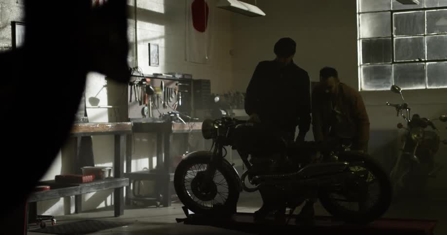 Two white men look over a motorcycle in a garage
