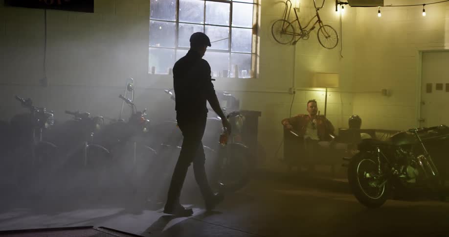 A man walks into the motorcycle garage smoking a cigar