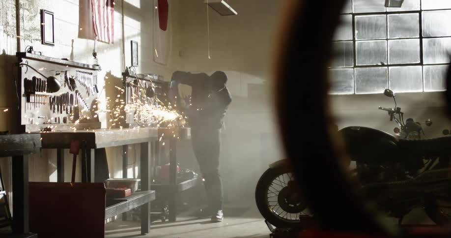Man uses power tool to cut metal on a workbench inside a motorcycle workshop