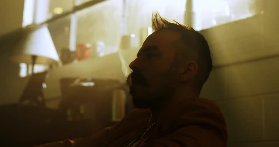 A white man sits indoors and smokes a cigar