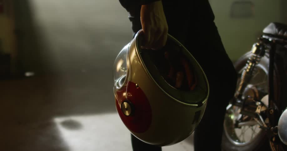 A white man holds on to a helmet while standing near a motorcycle