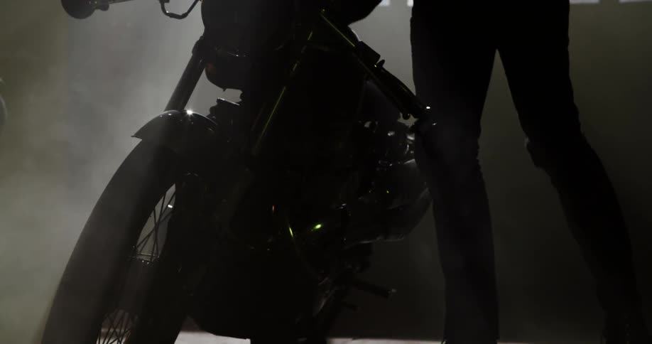 A white man dressed in black stands next to a motorcycle