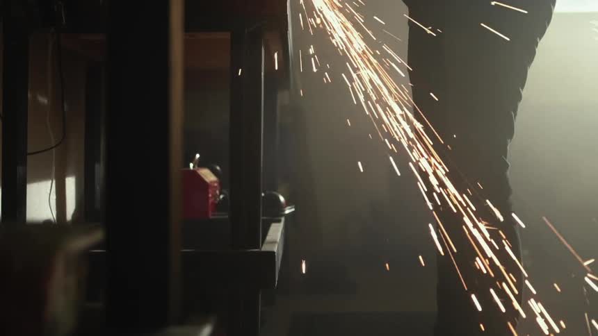 Man uses power tool to cut metal sheets on a workbench in a dimly lit workshop