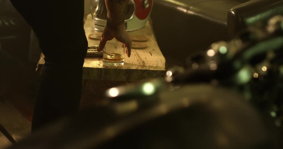 Man pours a glass of liquor in a room with a motorcycle
