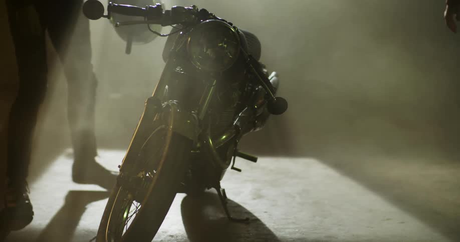 A person with a helmet kneeling down and touching a motorcycle while another person walks by
