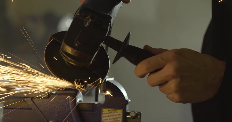 A white male uses a sander to grind down an object that throws sparks