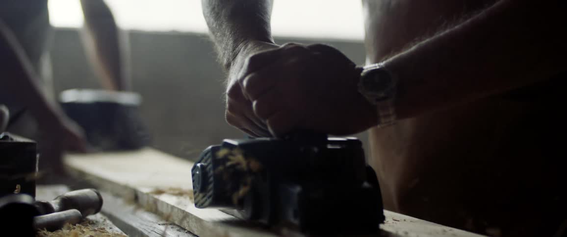 Sawdust flies as a man uses a sander on a piece of wood in a garage workshop