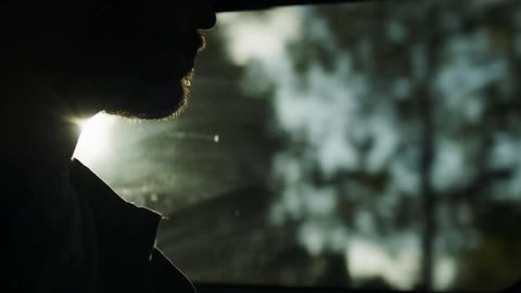 A man sits in a moving vehicle passing by a forested area