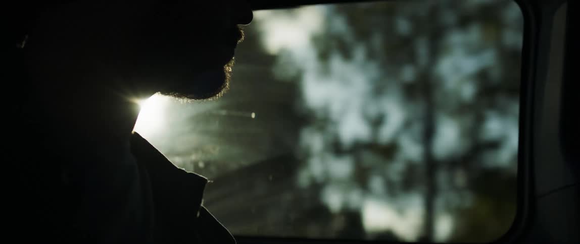 A man sits in a moving vehicle passing by a forested area