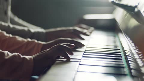 Two people sit and play the piano together