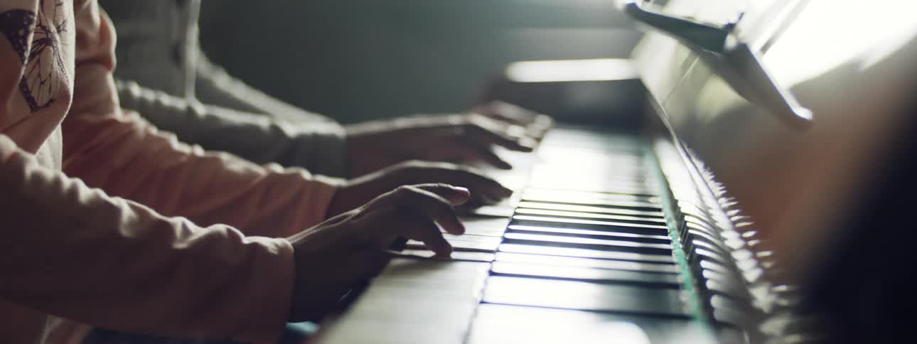 Two people sit and play the piano together