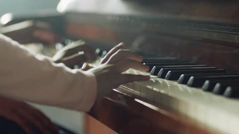 Two people sit at a piano and play together