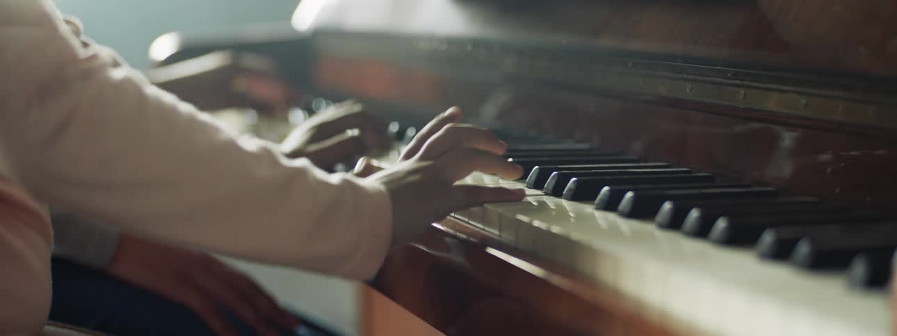 Two people sit at a piano and play together