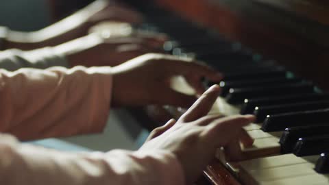 A man and a woman sit at a piano and play