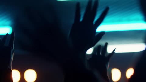 People hands waving in a concert with lights and a person on stage in the background